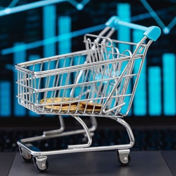 Carrito de compra en miniatura con monedas ante gráficos de ventas, rentabilidad al vender en marketplaces B2B